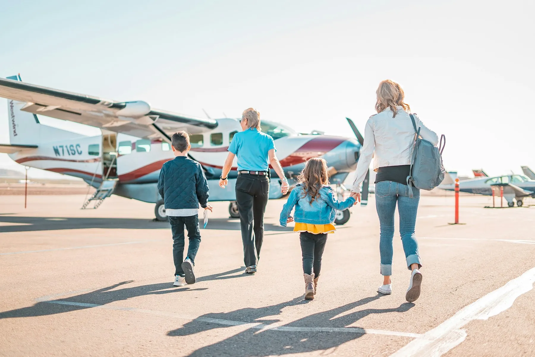 A family walking towards an aircraft on a sunny apron