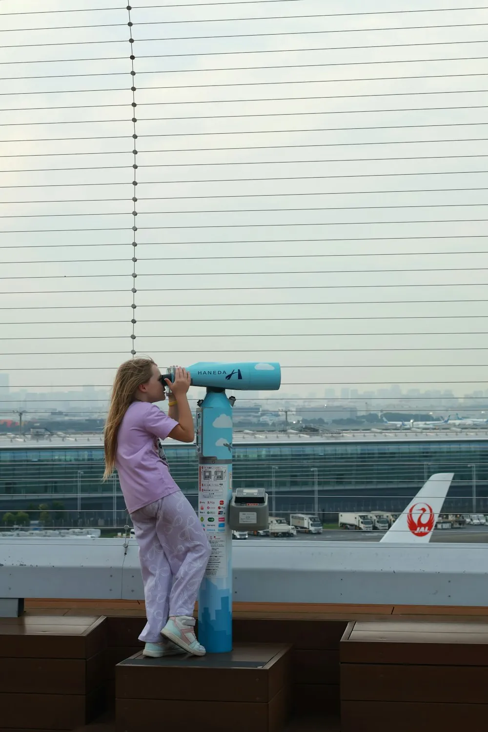 A child using an airport viewing telescope to spot planes