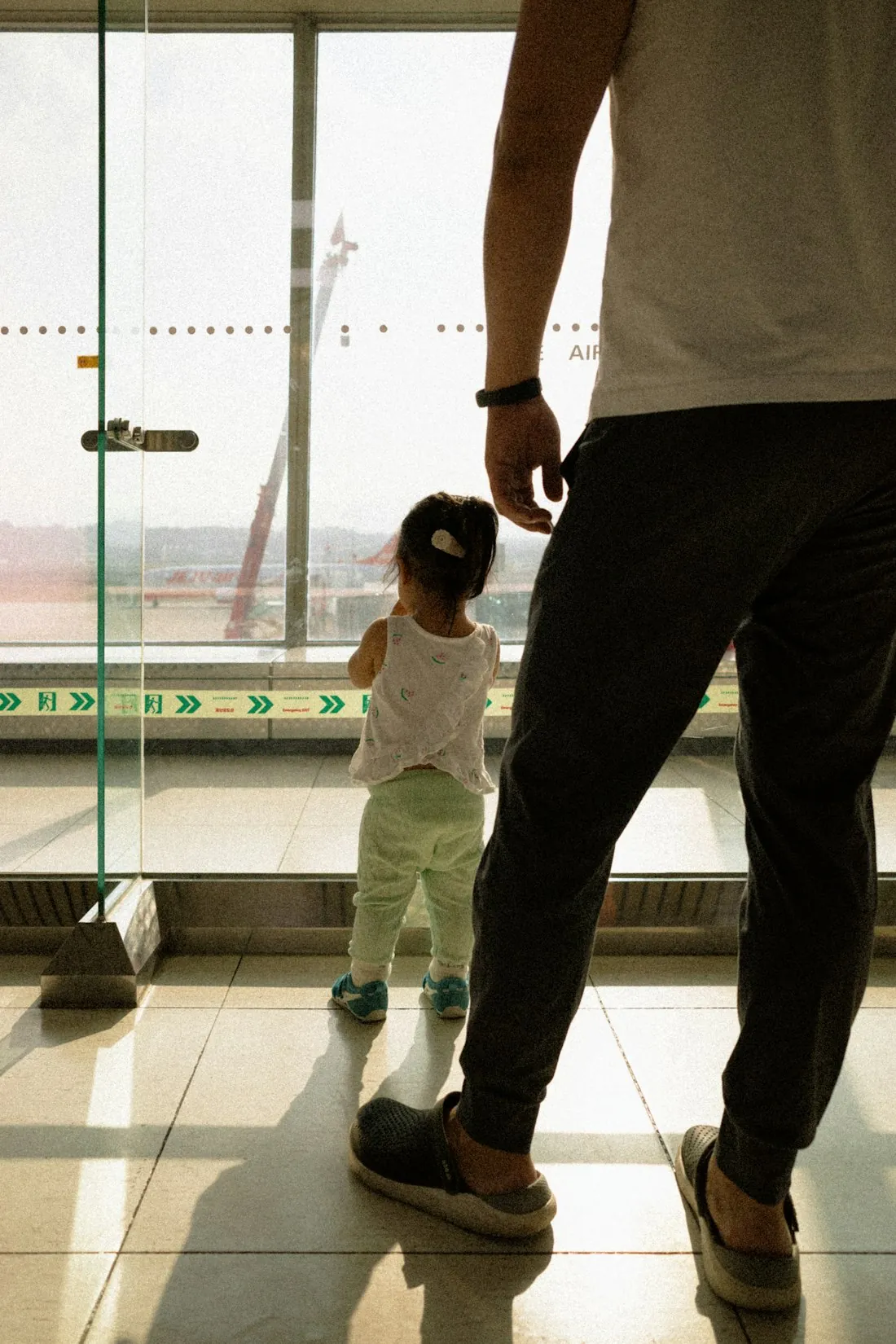 A parent and toddler watching a plane together through the terminal window